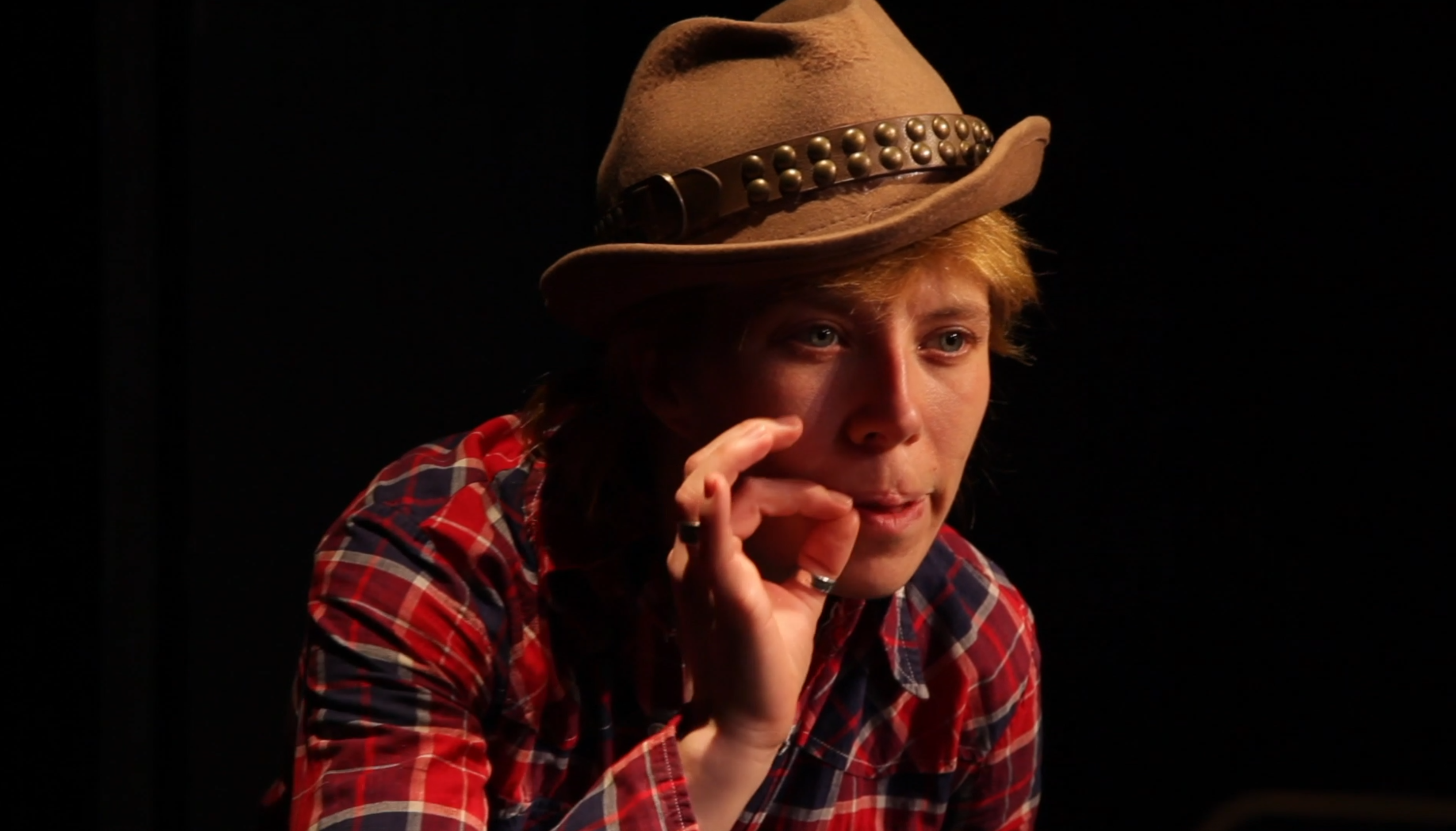A person with cowboy hat and red and black plaid shirt imitates smoking a cigarette