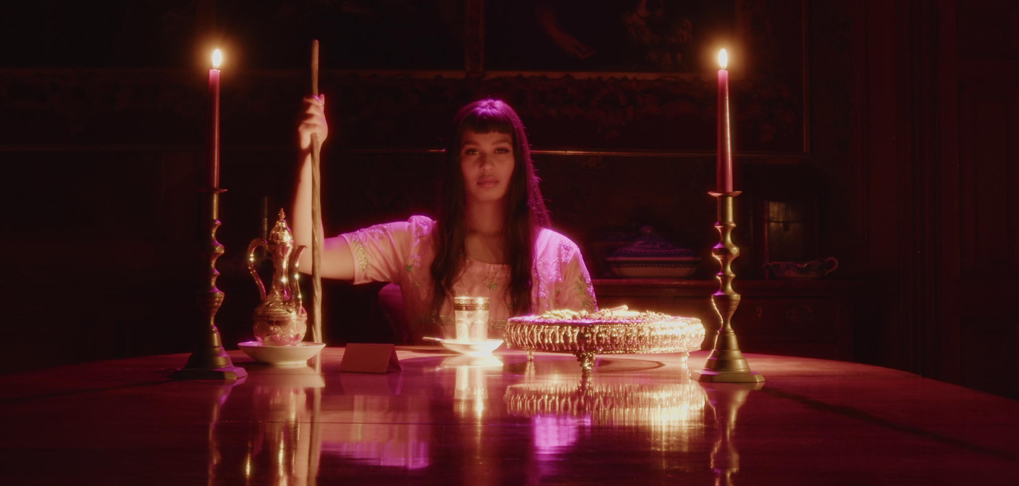 A south Asian woman sits at a dining table lit by pink light and candles