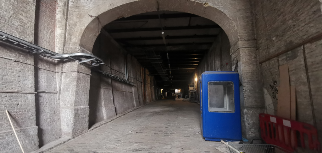 A photo of a deep brick tunnel which has an archway at the beginning and a light grey cobbled floor.