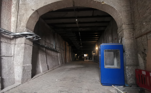 An image of a deep tunnel madeof brick with an archway at the beginning. The floor is made of grey cobbles.